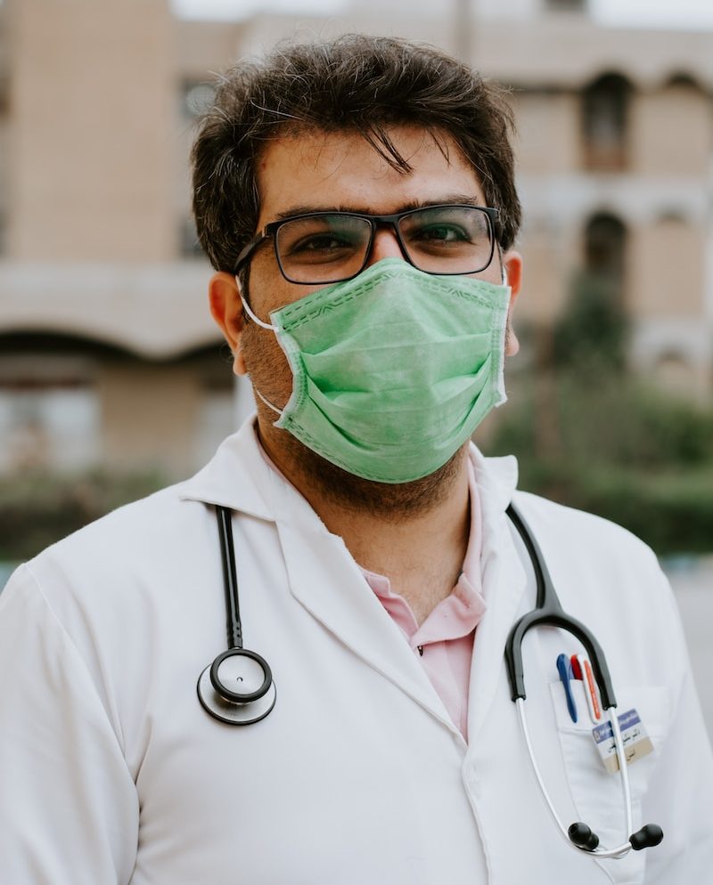 man in white scrub suit wearing green mask